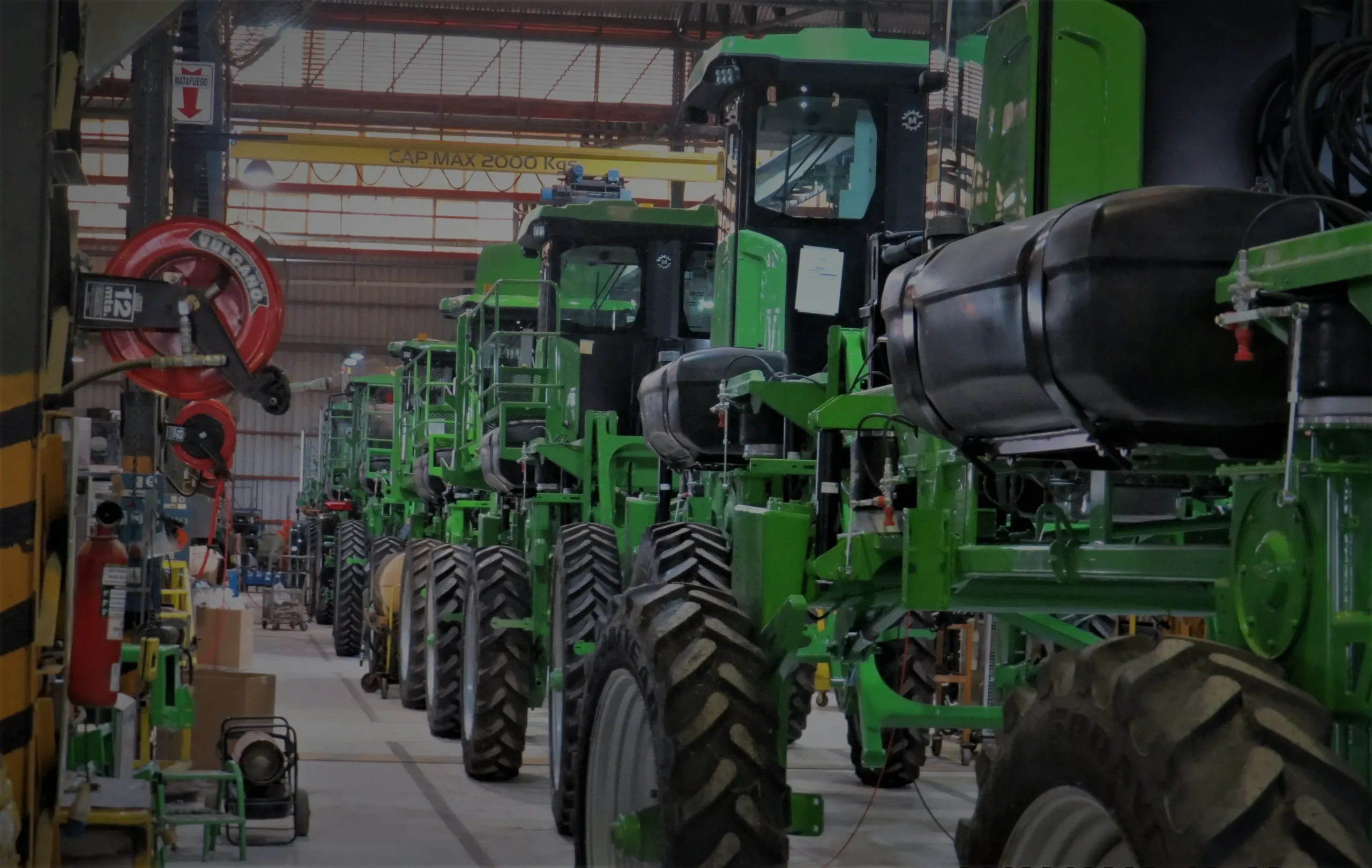 Green agricultural machinery lined up inside a manufacturing facility